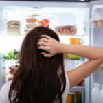 Confused Woman Searching For Food In An Open Refrigerator